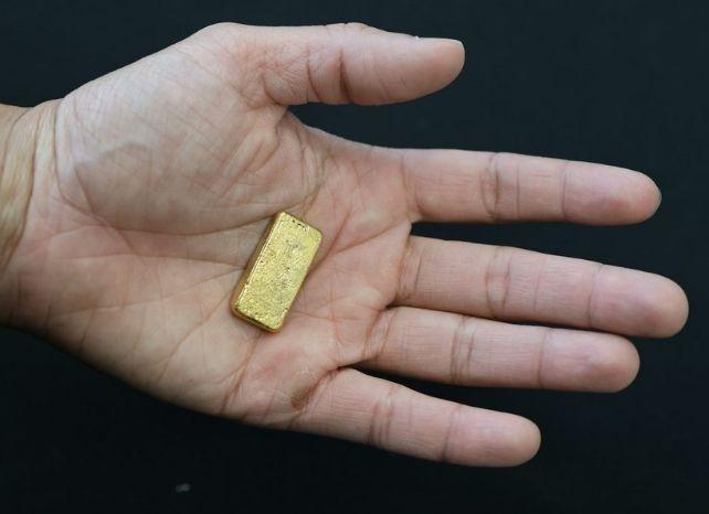 Persona che tiene un piccolo lingotto d'oro nel palmo della mano