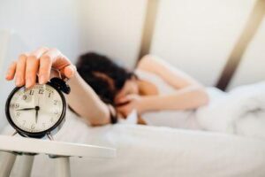 donna che si copre il viso mentre spegne la sveglia poco prima delle 6.45 del mattino