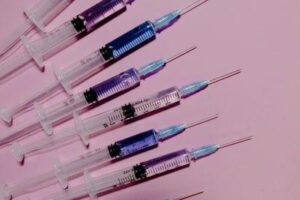 siringhe disposte su uno sfondo rosa; sono tutte rivolte verso l'angolo in alto a destra e contengono un liquido che è chiaro, blu pallido o viola pallido