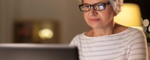 Felice donna anziana con occhiali che usa un laptop a casa di sera