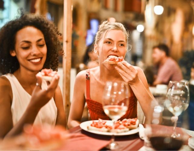 Due giovani donne che mangiano pizza e bevono vino