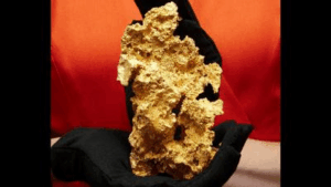 un nugget d'oro cristallino tenuto da qualcuno che indossa guanti neri