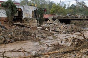 Una foto che mostra la devastazione delle inondazioni causate dall'uragano Helen. Mostra un fiume intasato da detriti e alberi caduti vicino a un edificio in rovina.