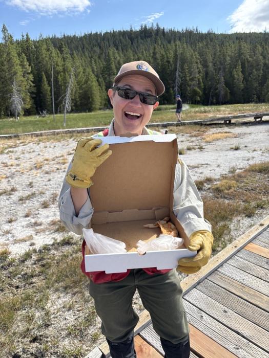 La volontaria del Programma di Geologia del Parco Nazionale di Yellowstone Tara Cross sorride e mostra una scatola di pizza trovata su Geyser Hill nel Bacino di Upper Geyser