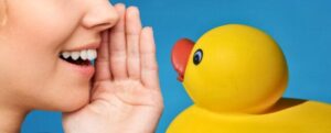 La bocca di una persona che parla oltre una mano a un'anatra di gomma