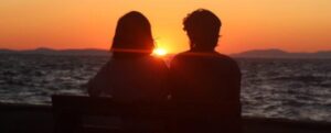 Silhouette di una coppia seduta su una panchina di fronte al mare durante il tramonto