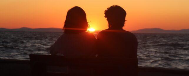 Silhouette di una coppia seduta su una panchina di fronte al mare durante il tramonto