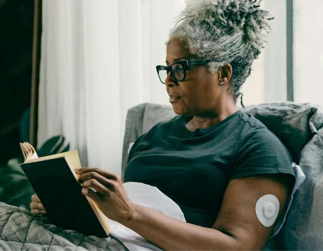 Donna con diabete che indossa un dispositivo CGM sul braccio mentre legge un libro