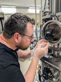Un uomo con occhiali che scruta in uno strumento scientifico.