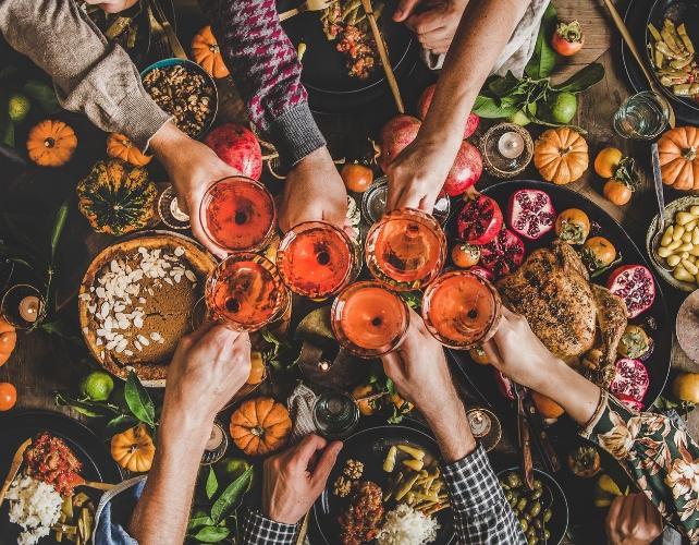 Vista aerea di cibo e più mani che tengono bicchieri di vino al centro dell'immagine