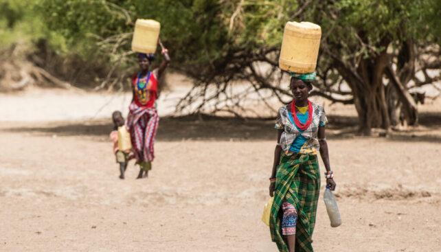 Due donne Turkana che trasportano acqua attraverso un paesaggio arido