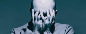 uomo calvo che si copre il viso