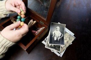 mani che frugano in una scatola di memorabilia d'infanzia con una pila di foto di neonati in bianco e nero sul tavolo accanto