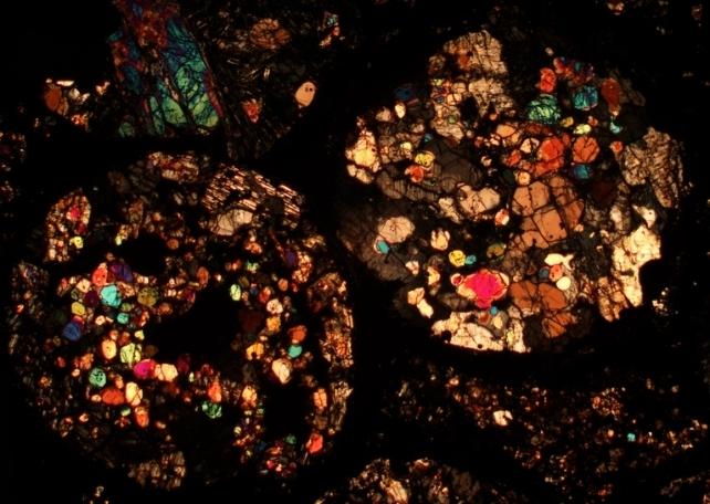 Blob riflettenti di colori brillanti che mostrano la composizione dei meteoriti da sottili fette sotto un microscopio