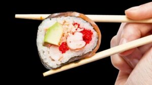 Mano che tiene le bacchette con sushi di avocado e frutti di mare