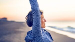 Donna che allunga le braccia verso l'aria su una spiaggia all'alba. Per illustrare la notizia che gli scienziati hanno trovato una molecola che simula i benefici dell'esercizio per rallentare l'invecchiamento