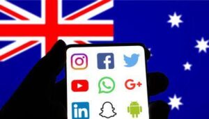 bandiera australiana con la silhouette di una mano umana davanti ad essa che tiene uno smartphone, contenente i loghi delle piattaforme di social media: instagram, facebook, il vecchio logo di twitter, youtube, whatsapp, google plus, linkedin, snapchat, e il logo android