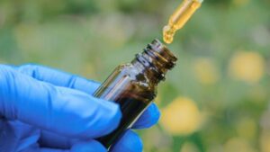 Mano guantata con olio in un contagocce sopra una bottiglia di ambra