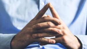 Immagine ad alto contrasto di un uomo in camicia blu, con le mani unite davanti al petto