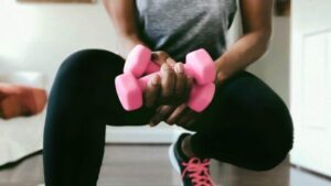 Una donna accovacciata, che tiene due pesi rosa brillanti in una mano.