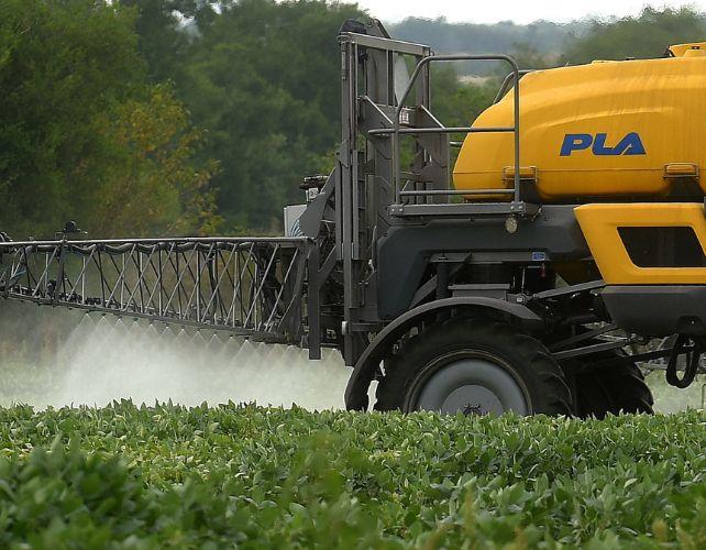 un trattore di dimensioni industriali fumiga un campo di soia con una fine nebbia