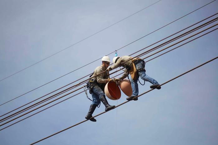 Due lavoratori su una linea elettrica che stanno posizionando un grande pallone di segnalazione