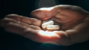 Primo piano di una mano che tiene 2 pillole bianche in capsule alla luce del sole, sfondo nero