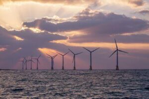 Un parco eolico offshore in mare con un tramonto dietro
