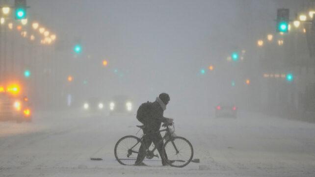 Una persona spinge una bicicletta attraverso una strada invernale tempestosa