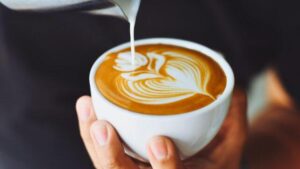 Le mani di un barista che versano un latte in una tazza bianca