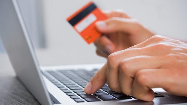 Mani che tengono una carta di credito mentre digitano su un laptop