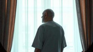 Uomo anziano in piedi vicino alla finestra che guarda fuori