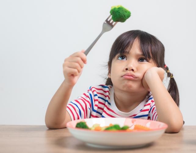 Un bambino confuso o scontroso che tiene un broccoli con una forchetta
