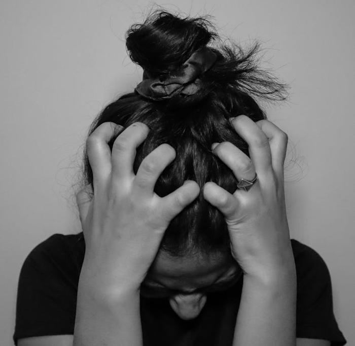 Una giovane donna appare stressata, tenendosi la testa tra le mani.