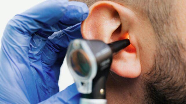 Primo piano di una mano guantata che tiene un dispositivo medico vicino all'orecchio di un paziente