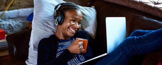 Giovane donna con le cuffie in videochiamata su laptop, bevendo un caffè