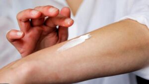 Primo piano di una persona che indossa una camicia bianca mentre applica crema sul braccio