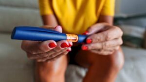 Persona con top giallo seduta su un divano e inclinata in avanti, che tiene una penna per insulina o farmaci