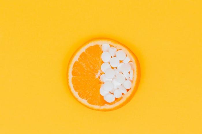 Un'arancia con metà che tiene compresse di vitamina C