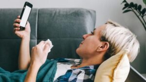donna sdraiata sul divano con il suo telefono e un fazzoletto