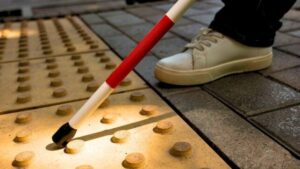 Un piede e un bastone, che si muovono lungo il marciapiede