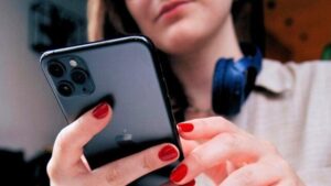 Vista dal basso di una persona con unghie dipinte di rosso, che tiene uno smartphone nero mentre guarda in basso
