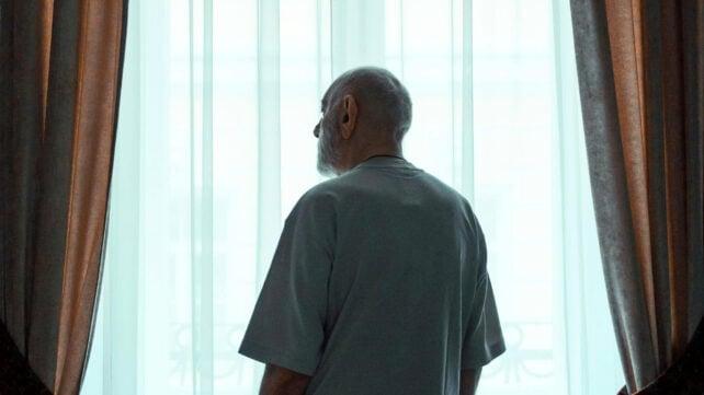 Uomo anziano in piedi vicino alla finestra che guarda fuori