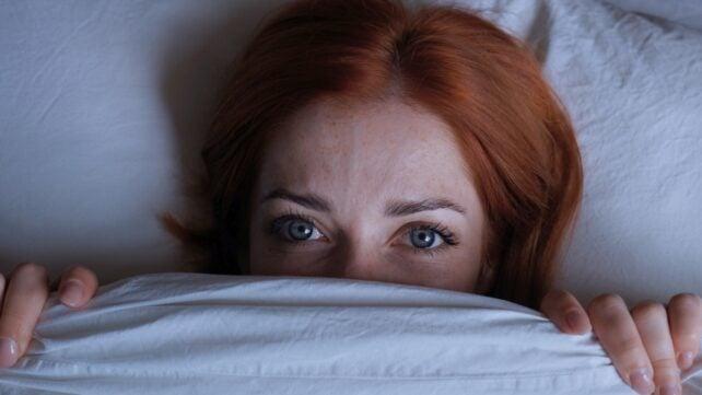 Donna insonne con capelli rossi sdraiata a letto nascosta sotto il piumone di notte