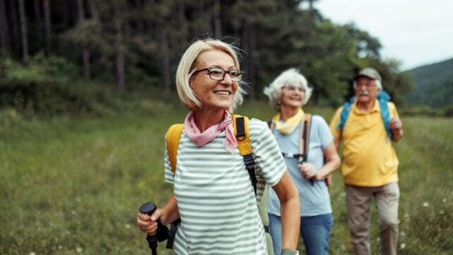 ThreeOlderPeopleWalkingInGrassyFieldBesideForest-642x361-1.jpg