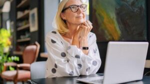 Una donna bionda più grande seduta a un tavolo in un caffè con un laptop