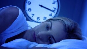 Donna sveglia a letto, con un orologio che segna le 3:15 del mattino sullo sfondo