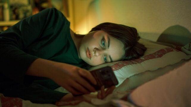 Un adolescente sdraiato a letto e che guarda lo schermo di un telefono