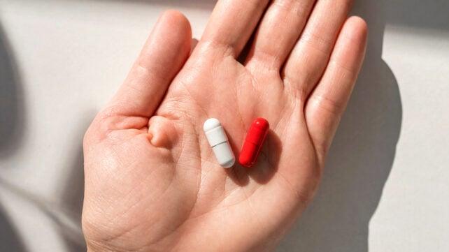 La mano di una donna che tiene pillole rosse su un tavolo bianco a casa. In primo piano.