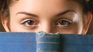 Gli occhi marroni di un giovane che sbirciano sopra il bordo di un libro aperto